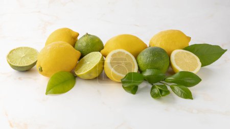 Citron frais et citron vert fruits entiers et tranchés avec des feuilles d'agrumes sur fond de table en marbre clair. Groupe d'agrumes et feuilles.