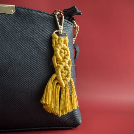 Close-up view of the handmade Macrame key chain hanging on the black hand bag isolated on the red background.