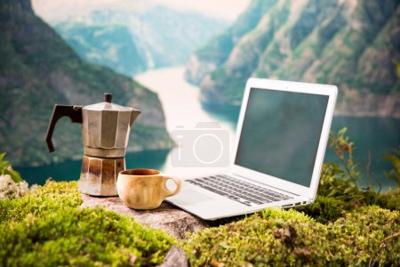 Ein freiberuflicher digitaler Nomaden-Morgenkaffee mit Moka-Kaffeemaschine, traditioneller finnischer Holztasse Kuksa und Laptop vor der skandinavischen Landschaft
