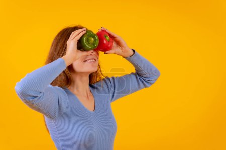 Photo for Vegetarian woman with spyglasses of peppers on her eyes on a yellow background, sticking out her tongue - Royalty Free Image
