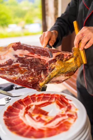 Photo for Detail of a man cutting Iberian ham at a wedding. Service of a person cutting a piece of ham. Chef or cutter with a knife cutting slices. traditional food of spain - Royalty Free Image