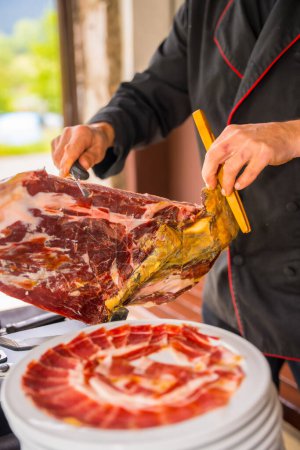 Photo for Detail of a man cutting Iberian ham at a wedding. Service of a person cutting a piece of ham. Chef or cutter with a knife cutting slices. traditional food of spain - Royalty Free Image