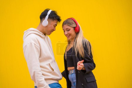 Multiethnic couple of Asian man and Caucasian woman on a yellow background, dancing bachata and salsa