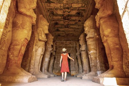 A young woman in a red dress at the Abu Simbel Temple next to the sculptures, in southern Egypt in Nubia next to Lake Nasser. Temple of Pharaoh Ramses II, travel lifestyle