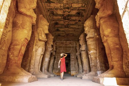 A young woman in a red dress at the Abu Simbel Temple next to the sculptures, in southern Egypt in Nubia next to Lake Nasser. Temple of Pharaoh Ramses II, travel lifestyle