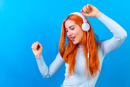 Redhead woman in studio photography smiling dancing on a blue background