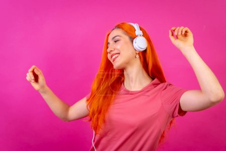Redhead woman in studio photography dancing smiling on a pink background