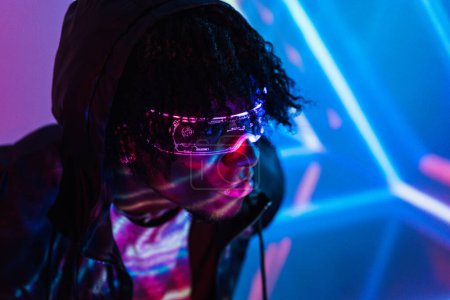 Studio portrait with purple and blue neon lights of an afro futuristic man wearing artificial intelligence goggles