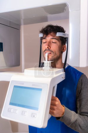 Téléchargez les photos : Photo verticale d'un homme les yeux fermés dans une machine à rayons X dentaire - en image libre de droit