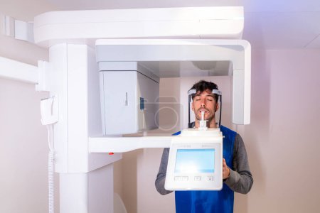 Téléchargez les photos : Vue frontale d'un patient masculin les yeux fermés dans une machine à rayons X dentaire - en image libre de droit