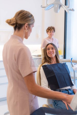Foto de Foto vertical de una dentista de belleza hablando con una paciente sentada en la clínica - Imagen libre de derechos