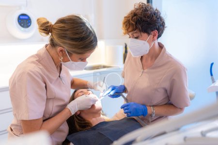 Foto de Dentista y asistente examinando la boca de un paciente acostado en la silla de una clínica - Imagen libre de derechos