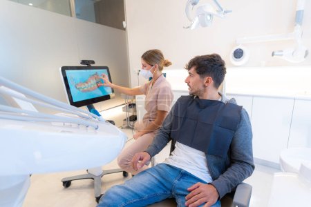Dentista usando tecnología moderna para explicar el procedimiento dental a un hombre sentado en la clínica
