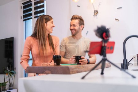Foto de Foto frontal de una feliz pareja joven que fluye en línea desde casa mientras bebe café - Imagen libre de derechos