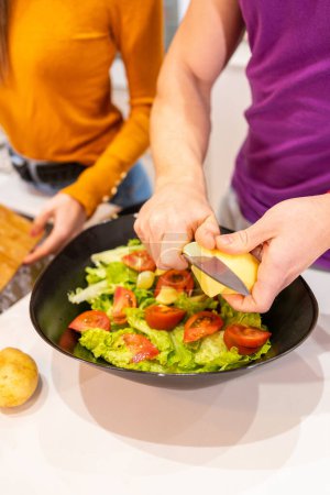 Photo for Vertical photo with close-up of a man cutting ingredients for a salad next to his partner at home - Royalty Free Image