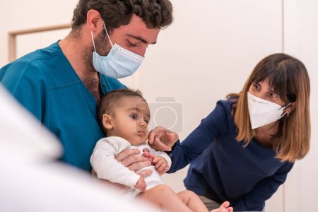 Foto de Médico sosteniendo a un bebé junto a su madre durante un examen médico - Imagen libre de derechos