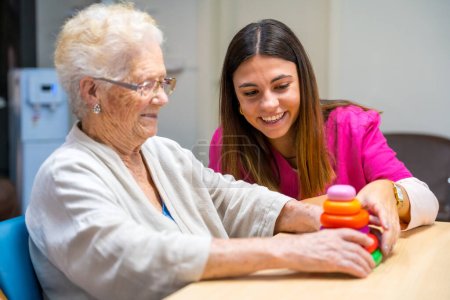 Enfermera linda ayudando a una mujer a jugar juego de habilidad de mesa en un hogar de ancianos