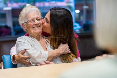 Foto de Feliz momento de una anciana y enfermera abrazándose y besándose en un geriátrico - Imagen libre de derechos