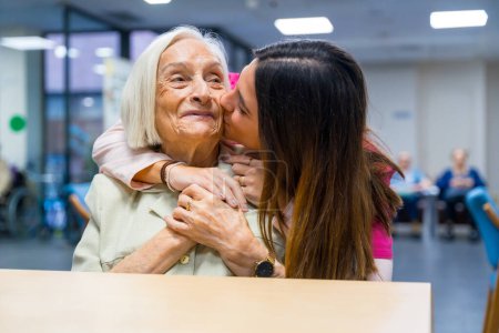 Foto de Enfermera besándose y abrazando desde la espalda a una linda anciana en un geriátrico - Imagen libre de derechos