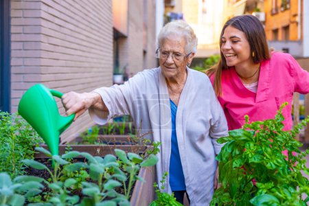 Foto de Enfermera y anciana regando plantas herbales en el huerto urbano un hogar de ancianos - Imagen libre de derechos