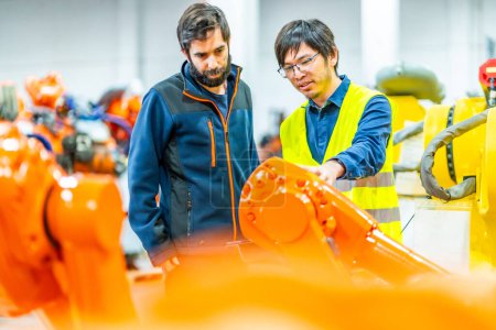 Foto de Equipo internacional de ingenieros que controlan la línea de montaje de una fábrica de fabricación de robótica - Imagen libre de derechos