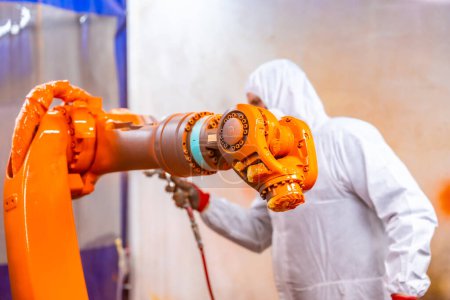 Foto de Pintor industrial con equipo protector pintando un brazo robótico con spray en una industria de robots industriales - Imagen libre de derechos