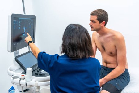 Paciente sentado en camilla mientras el cardiólogo realiza un ecocardiograma en el hospital