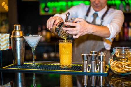 Photo for Close-up of a bartender preparing a cocktail with orange juice in a luxury bar - Royalty Free Image
