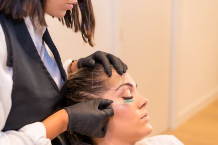 Téléchargez les photos : Gros plan d'un coiffeur peignant les cils d'un client assis les yeux fermés sur une chaise dans un salon de beauté - en image libre de droit