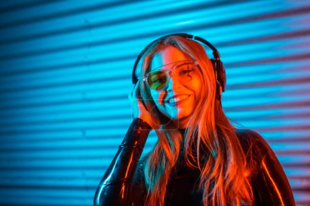 Photo for Smiley disc jockey using headphones in an urban space with blue and red neon lights - Royalty Free Image