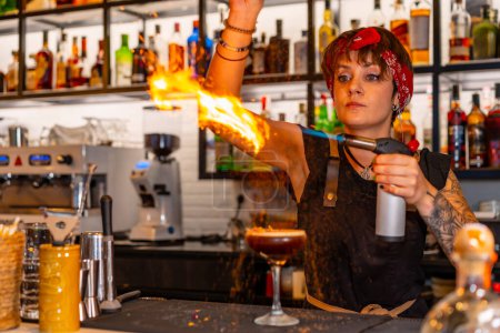 Photo for Bartender using torch to flaming the decoration of a cocktail in the counter of a bar - Royalty Free Image