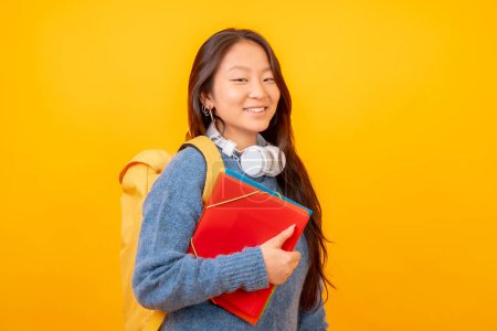 Foto de Estudio foto con fondo amarillo de un estudiante chino con auriculares, bolsa y carpetas - Imagen libre de derechos