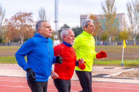 Foto de Hombres deportivos senior con ropa deportiva colorida corriendo juntos en un campo de atletismo - Imagen libre de derechos