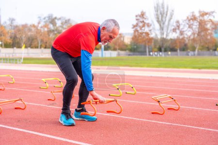 Photo for Sportive senior man placing starting blocks on an athletics track in winter - Royalty Free Image