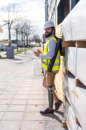 Photo for Vertical side view portrait of an engineer with prosthetic leg working in a construction site outdoors - Royalty Free Image