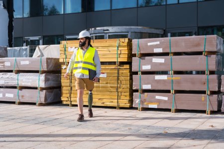 Photo for Engineer with prosthetic leg walking along the street next to the construction site - Royalty Free Image