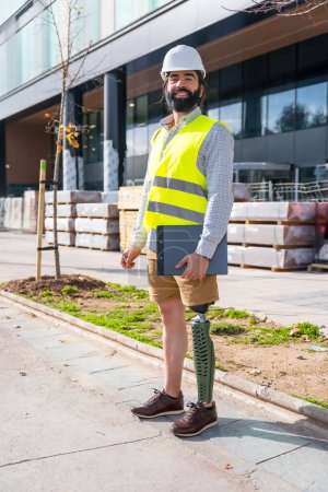 Photo for Vertical portrait of an employee with prosthetic leg working on construction site wearing protective equipment - Royalty Free Image
