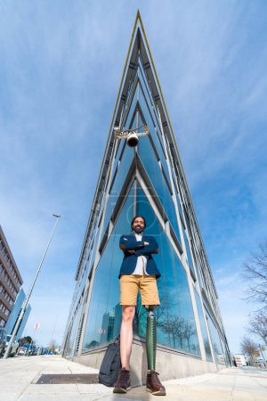 Photo for Vertical portrait with low angle view of a businessman with prosthetic leg in the city outside office building - Royalty Free Image