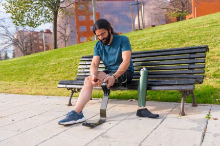 Photo for Physically disabled man adjusting prosthetic leg before running sitting on an urban park bench - Royalty Free Image