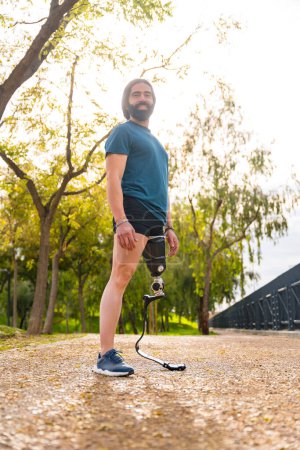 Photo for Vertical portrait of a proud sportsman with prosthetic leg standing in a park - Royalty Free Image