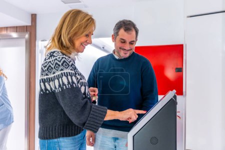 Foto de Pacientes sonriendo mientras programan citas en el hospital usando una máquina moderna en la sala - Imagen libre de derechos