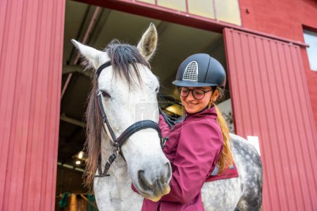 Téléchargez les photos : Vue en angle bas d'une jeune femme jockey caressant son cheval à l'extérieur de l'écurie - en image libre de droit