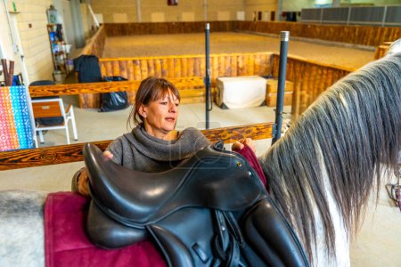 Photo for High angle view of a woman saddling a horse in stable - Royalty Free Image