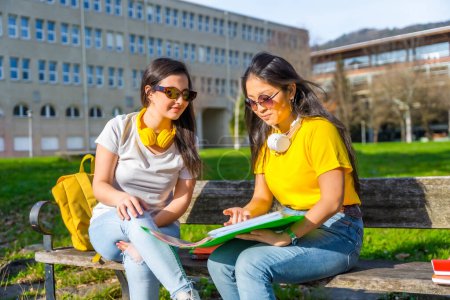 Téléchargez les photos : Étudiants multiethniques avec écouteurs regardant leurs devoirs assis sur le banc d'un campus - en image libre de droit