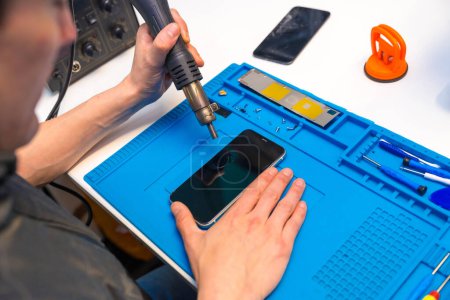 Téléchargez les photos : Vue de dessus d'un technicien attachant les parties d'un téléphone portable à l'aide d'un fer à souder dans un atelier - en image libre de droit