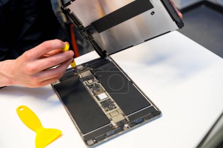 Close-up top view of a male worker using screwdriver to fix a digital tablet in a workshop