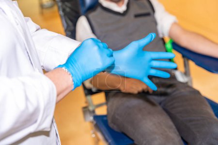 Téléchargez les photos : Gros plan d'une infirmière méconnaissable se préparant à enfiler des gants bleus chirurgicaux pour faciliter un don de sang - en image libre de droit