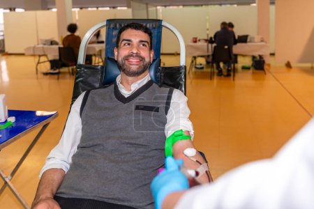 Altruist smiling man sitting on comfortable chair while donating blood in a pavilion