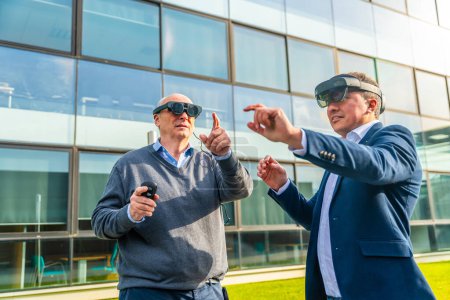 Téléchargez les photos : Homme d'affaires âgé avec un collègue portant un simulateur de réalité virtuelle gestuelle au quartier financier - en image libre de droit