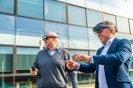 Téléchargez les photos : Hommes d'affaires seniors et matures utilisant le casque VR avec des actions à l'extérieur à côté d'un bâtiment financier - en image libre de droit